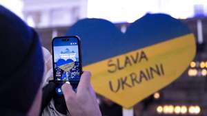 epa12773852 A person takes a picture of a sign in the colours of the Ukrainian flag reading 'Glory to Ukraine!' during a rally marking the fourth anniversary of the Russian invasion of Ukraine, at the Senate Square in Helsinki, Finland, 24 February 2026. Ukraine marks the fourth anniversary since Russia began its full-scale invasion of the country in 2022.  EPA/JUSSI ESKOLA