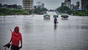 epa11300394 People walk past vehicles stuck in a flooded street in Jangwani, Dar Es Salaam, Tanzania, 25 April 2024. Tanzania Prime Minister Kassim Majaliwa said at least 155 people have died in Tanzania as torrential rains linked to El Nino weather phenomenon caused flooding and landslides, affecting about 200,000 people.  EPA/DIEGO MENJIBAR