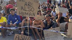 epa13176333 Migrants hold signs that read 'We are also human' and 'Asylum' during a hunger strike at the El Trampolin beach campsite in Ceuta, Spain, 17 August 2026. The migrants entered the Spanish enclave from Morocco during the mass border crossings that began on 30 July.  EPA/LAURA RINCON
