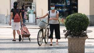 Mulher circula bicicleta pela mao na rua com máscara na cara no centro de Macau, China, 22 de agosto de 2023. GONÇALO LOBO PINHEIRO/LUSA
