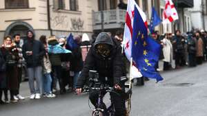 epa11796068 A protester rides a bicycle with EU and Georgian flags near supporters of the Georgian opposition during a protest action in Tbilisi, Georgia, 28 December 2024. Georgian lawmakers elected Mikheil Kavelashvili as the country's new president on 14 December in a controversial parliamentary vote that sparked accusations of illegitimacy and protests. Kavelashvili will be inaugurated as President of Georgia on 29 December 2024.  EPA/DAVID MDZINARISHVILI