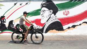epa13165935 An Iranian man passes with his bike next to a wall painting featuring late Iranian supreme leader Ayatollah Ali Khamenei in a street in central Tehran, Iran, 13 August 2026. Tensions between Iran and the US remain high as opposing claims persist over shipping control in the Strait of Hormuz.  EPA/ABEDIN TAHERKENAREH RESTRICTIONS: NO Access Israel Media/Persian Language TV Stations Outside Iran/Strictly No Access BBC Persian/VOA Persian/Manoto TV/Iran International TV. (As mandated by Iran's Directorate General for Foreign Media) --