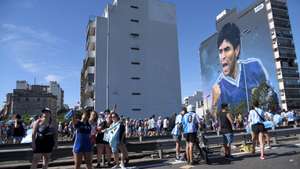 epa10375178 Fans of Argentinian national soccer team celebrate during the victory parade of the Argentinian national soccer team in Buenos Aires, Argentina, 20 December 2022 as a mural depicting soccer legend Diego Maradona of Argentina is seen. Argentina defeated France 4-2 in a penalty shoot-out after a 3-3 draw to win the FIFA World Cup 2022 soccer tournament. The parade was stopped early because the streets were overflowing with fans and the Argentine team had to return to the sports venue of the Argentine Football Association (AFA) located in Ezeiza by helicopter.  EPA/Enrique GarcÃ­a Medina