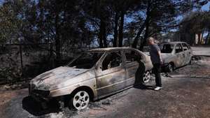 epa10082423 A woman looks at burnt cars after wildfire at the north-east suburb of Anthousa, near Athens, Greece, 20 July 2022. The Penteli fire appears to be subsiding, with no active fronts and all forces now working to extinguish minor small blazes and to prevent any danger of a rekindling of the flames, according to the latest update on 20 July afternoon from the civil protection service's coordination centre.  EPA/GEORGE VITSARAS