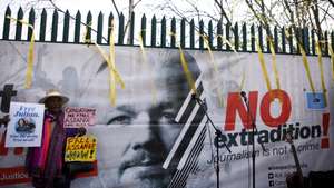 epaselect epa09844244 An activist holds placards calling for the release of Julian Assange beside a banner featuring Assange's face as well wishers gather outside HMP Belmarsh to celebrate the wedding of Stella Moris and Assange in London,  Britain, 23 March 2022.  Assange is in prison facing extradition to the United States, where he is wanted over an alleged conspiracy to obtain and disclose national defence information.  EPA/DAVID CLIFF