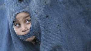 Criança espreita através de um buraco da lona do seu abrigo, Faixa de Gaza, Palestina