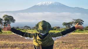 Homem de braços abertos com o Kilimanjaro ao fundo.
