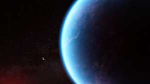 Illustration of an exoplanet planet and its red cool dwarf star on a black background that is speckled with some small stars. The planet is large, in the foreground on the right and the star is smaller, in the background at the lower left. The planet is various shades of blue, with wisps of white scattered throughout. The left edge of the planet (the side facing the star) is lit, while the rest is in shadow. The star has a bright red glow.