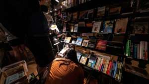 A woman browses the books on a bottom shelf.Crowds of