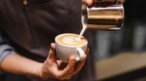 close up view of Young woman preparing a coffee by drawing a flower with milk