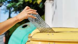Close up shot of a hand throwing a used plastic bottle into the yellow garbage can for recycling.