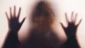 Domestic abuse victim with hands pressed against glass window