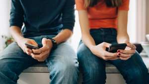 Midsection of male and female friends using mobile phones while sitting at kitchen counter