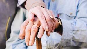 Close-up of old man&#039;s and woman&#039;s hands resting on a cane