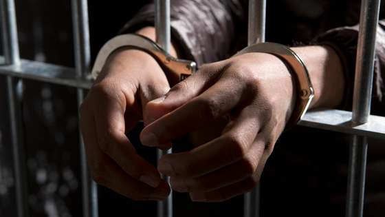 A prisoner behind bars with hands cuffed