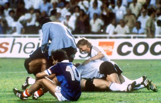 SEVILLA, SPAIN - JULY 8:  West German players celebrate after forward Horst Hrubesch scored the winning penalty kick in extra time as French midfielder Michel Platini sits on the field 08 July 1982 in Sevilla during the World Cup semifinal soccer match between West Germany and France. West Germany beat France 5-4 on penalty kicks (1-1 at the end of regulation time; 3-3 at the end of extra time).  AFP PHOTO  (Photo credit should read STAFF/AFP/Getty Images)