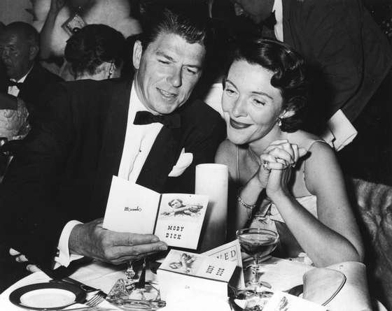 American actor Ronald Reagan and his wife Nancy Reagan sit at a restaurant table, looking at a brochure at the premiere party for the film, 'Moby Dick,' directed by John Huston, 1956. (Photo by Hulton Archive/Getty Images)