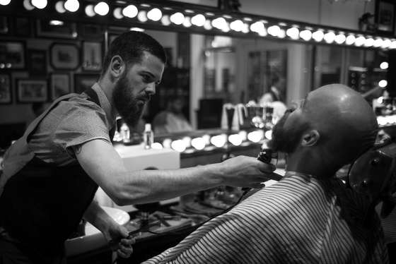 MANCHESTER, ENGLAND - APRIL 29: (EDITORS NOTE: This image has been converted to black and white. Colour version available upon request.) Barber Ricky Trim wet shaves a customer in Manchester's Barber Barber, a 'gentleman's saloon' style male barber shop, on April 29, 2015 in Manchester, England. According to owner Johnny the Baba, Barber Barber is the UK's finest barber shop. The shop for 'gentleman and scoundrels' takes a traditional approach to male grooming, and offers services such as wet shaving, beard scultping and highly skilled hair styling. The shop also offers complimentary drinks and cigars to it's customers and operates a 'gentlemen only' door policy. (Photo by Christopher Furlong/Getty Images)