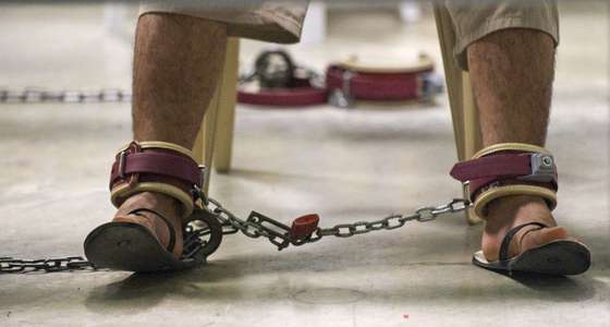 A detainee sits wearing restraints as he reads during a life skills class that includes resume writing inside Camp VI at Guantanamo Bay, Cuba, March 30, 2010. AFP Photo/Paul J. Richards (Photo credit should read PAUL J. RICHARDS/AFP/Getty Images)