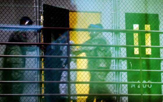 This image reviewed by the US military shot through a one way mirror shows guards moving a detainee from his cell in Cell Block A of the "Camp Six" detention facility of the Joint Detention Group at the US Naval Station in Guantanamo Bay, Cuba, January 19, 2012. AFP PHOTO/Jim WATSON (Photo credit should read JIM WATSON/AFP/Getty Images)