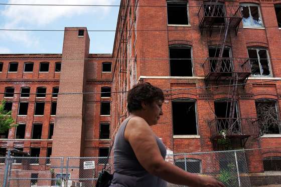 WATERBURY, CT - MAY 20: A woman walks by a closed factory on May 20, 2013 in Waterbury, Connecticut. Waterbury, once a thriving industrial city with one of the largest brass manufacturing bases in the world, has suffered economically in recent decades as manufacturing jobs have left the area. According to recent census data, 20.6%. of the city's residents are living below the poverty level. (Photo by Spencer Platt/Getty Images)