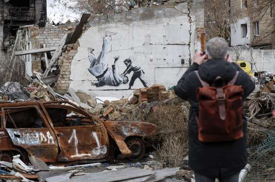 epaselect epa10303646 A man takes a picture of a mural depicting child overthrowing a man in judo clothes, in a style resembling the works of British street artist Banksy, at a wall of a building that was destroyed during shelling in Borodyanka, Ukraine, 13 November 2022. A photo of a mural in Borodyanka depicting a gymnast was shared by Banksy on his social media channel on 11 November, while other works attributed to him in different locations in Ukraine and resembling Banksy's style have not been shared on the artist's channel yet. Russian troops entered Ukraine on 24 February 2022, starting a conflict that has provoked destruction and a humanitarian crisis. EPA/SERGEY DOLZHENKO