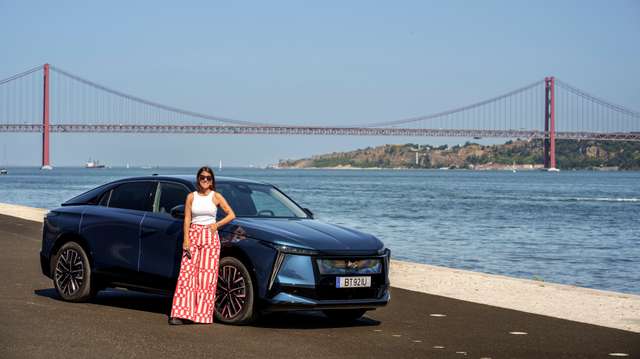 Bárbara Tomaz posa ao lado do automóvel DS com a ponte 25 de abril ao fundo.