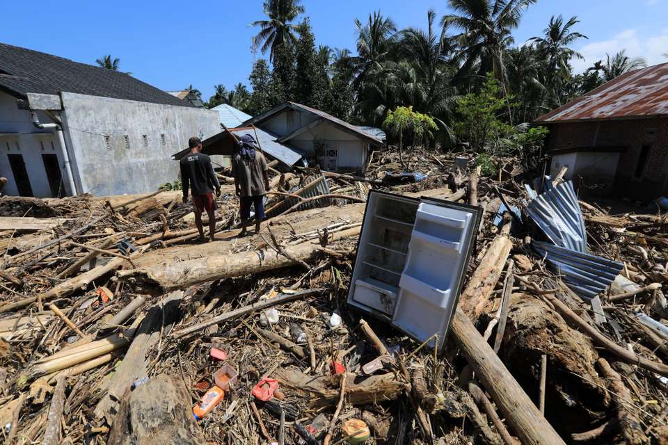 epa12561474 Residents walk among large piles of wood that were swept away by the floodwaters in a flood-affected village in the Meureudu area, Pidie Jaya Aceh, Indonesia, 01 December 2025. According to National Disaster Management Agency Floods and landslides triggered by Tropical Cyclone Senyar have killed at least 442 people across Aceh, North Sumatra, and West Sumatra provinces. This number is expected to rise, as approximately 402 people remain uncounted for.  EPA/HOTLI SIMANJUNTAK