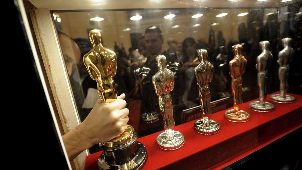 Um membro do staff faz ajustes para colocar uma estátua dos Oscares junto das outras na Academia