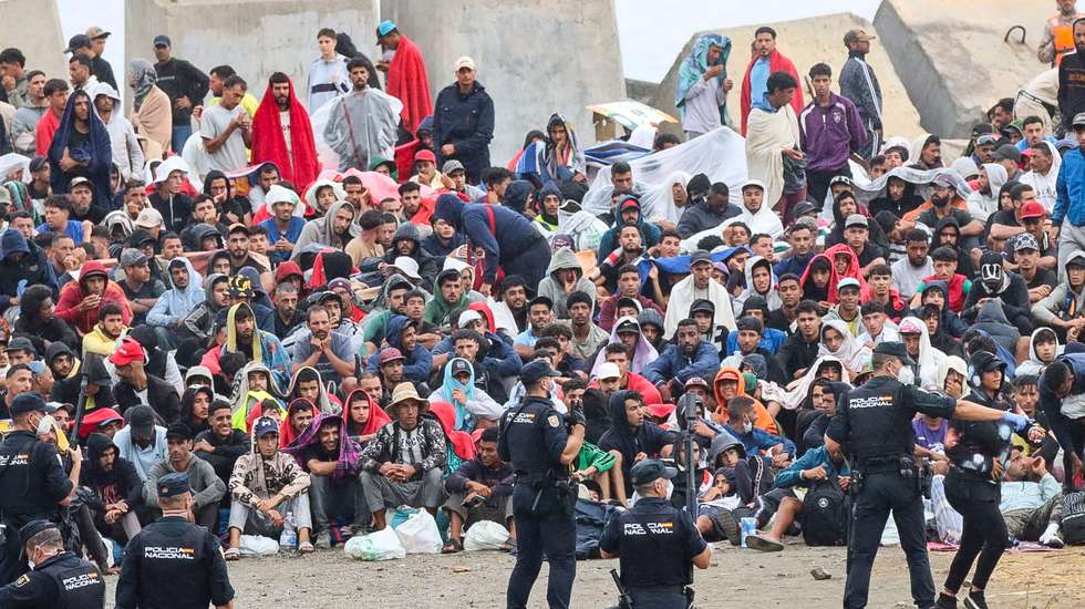 epaselect epa13182348 Several policemen stand guard near a group of migrants at El Trampolin beach in Ceuta, Spain, 21 August 2026. Authorities in Spain's North African enclave of Ceuta cleared migrants from El Trampolin beach for the second time on 21 August, grouping them in one area while crews cleaned the site. The Spanish government is providing temporary shelter for 1,800 migrants sleeping rough on Trampolin Beach and in the Loma Colmenar area of Ceuta, and plans to gradually expand these facilities.  EPA/REDUAN