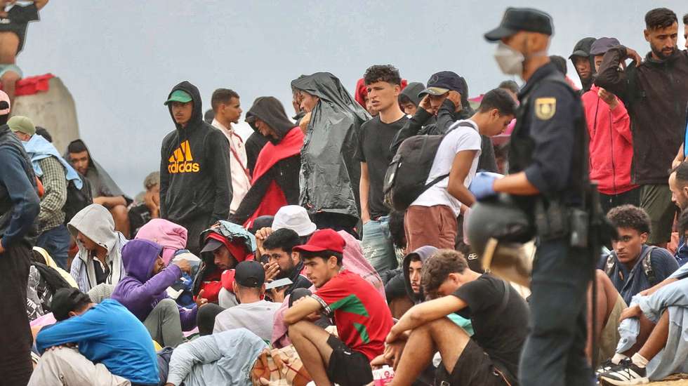 epa13182414 Several policemen stand guard near a group of migrants at El Trampolin beach in Ceuta, Spain, 21 August 2026. Authorities in Spain's North African enclave of Ceuta cleared migrants from El Trampolin beach for the second time on 21 August, grouping them in one area while crews cleaned the site. The Spanish government is providing temporary shelter for 1,800 migrants sleeping rough on Trampolin Beach and in the Loma Colmenar area of Ceuta, and plans to gradually expand these facilities.  EPA/REDUAN