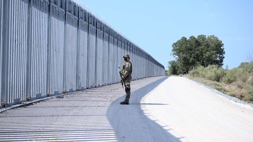 epa09440117 A soldier stands in front of a steel fence built along the Evros River in the area of Feres, at the Greek-Turkish border, Greece, 01 September 2021. The fence was built to prevent the illegal arrival of migrants into Greek territory.  EPA/DIMITRIS ALEXOUDIS