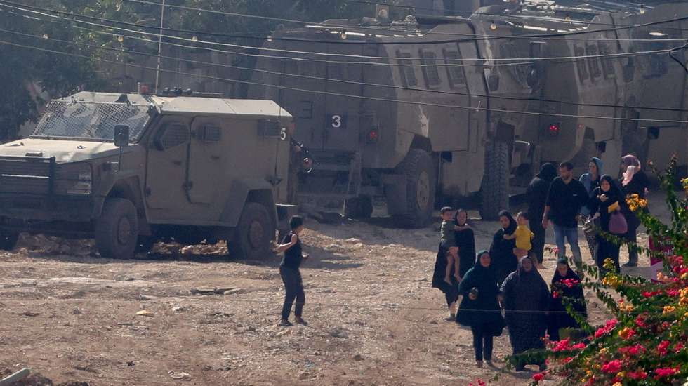 epa11575425 Palestinians, among them women and children, walk past Israeli troops as they leave Jenin refugee camp during heavy clashes on the fourth day of an Israeli military operation in the West Bank city of Jenin, 31 August 2024. According to the Palestinian Health Ministry, at least 20 Palestinians have been killed since Israeli military operations started on 28 August 2024 in the West Bank cities of Tulkarem, Jenin and Tubas. The Israeli army said that it's conducting a large-scale counter-terrorism operation in several areas. More than 40,000 Palestinians and over 1,400 Israelis have been killed, according to the Palestinian Health Ministry and the Israel Defense Forces (IDF), since Hamas militants launched an attack against Israel from the Gaza Strip on 07 October 2023, and the Israeli operations in Gaza and the West Bank which followed it.  EPA/ALAA BADARNEH