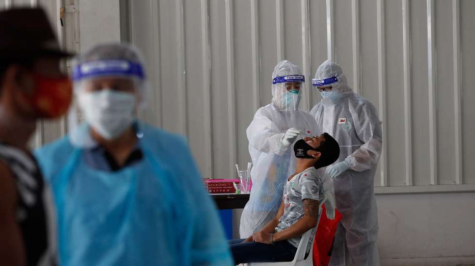 epa09027154 A Myanmar migrant worker (L) lines up as health officials wearing protective suits collect a sample from a man during a COVID-19 nasal swab test as an effort to stop the spread of the outbreak cluster at Bang Yai market, Nonthaburi province, Thailand, 21 February 2021. A Thai doctor had caught the disease and died after treating patients infected with COVID-19 coronavirus pandemic raising the death toll in Thailand to 83 with 25,415 infections. Thailand is battling with the rise of new COVID-19 coronavirus pandemic infections since December 2020 while the first batch of 200,000 doses of vaccine against COVID-19 coronavirus supplied by China's Sinovac Biotech are due to arrive on 24 February 2021 and will follow by 800,000 in March and million in April with another order of 61million doses from AstraZeneca expected to arrive in May to secure enough COVID-19 vaccination for the country's entire population. Thailand is already behind its regional neighboring countries of the inoculation.  EPA/RUNGROJ YONGRIT