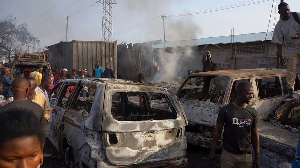 epa09567859 Sierra Leone residents of Freetown look at burned vehicles in the aftermath of an explosion at a junction outside Choithram Supermarket in Freetown, Sierra Leone, 06 November 2021.  At least 99 people have died following a massive fuel tanker explosion in the capital Freetown, after a fuel tanker collided with a truck.  EPA/MOHAMED KONNEH