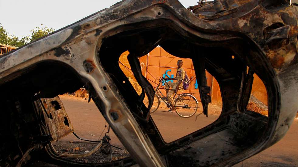 epaselect epa04474287 A boy from Burkina Faso cycles past burned vehicles damaged during violent demonstrations by pro democracy protesters that led to the resignation of President Blaise Compaore in Ouagadougou, Burkina Faso, 03 November 2014. President Blaise Compaore resigned on 31 October 2014 following the violent protests against his bid to change the constitution to extend his rule of 27 years. After a brief claim to power by army General Honore Traore a power struggle ensued with Presidential guard commander Lieutenat-Colonel Isaac Zide being appointed as transitional leader. Thousands of protesters took to the Place de la Nation on 02 November in protest against the military rule.  EPA/LEGNAN KOULA