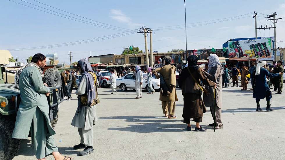 epa09421845 Taliban fighters stand guard as Afghans gather outside the Hamid Karzai International Airport to flee the country, in Kabul, Afghanistan, 20 August 2021. The Afghan interim council, formed to assist in the power transfer following President Ashraf Ghani's escape, has met several Taliban leaders to discuss issues related to control and security during the transition process. Fighting and violence have significantly reduced in Afghanistan with the surrender of the government troops and the resounding victory of the Taliban.  EPA/STRINGER