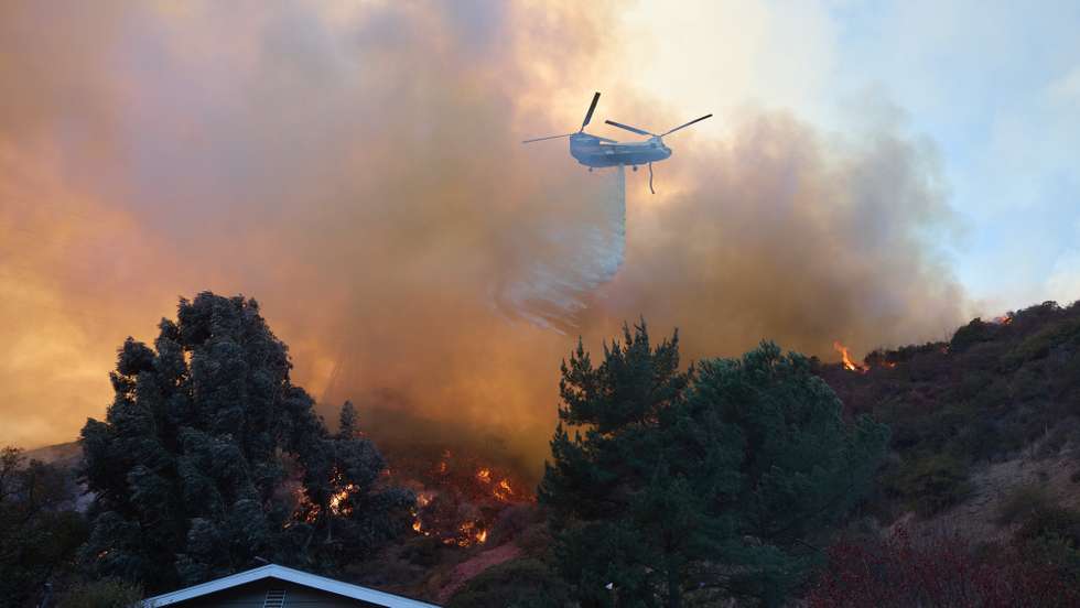 epaselect epa11819202 A helicopter does a water drop over a home during the Palisades wildfire in Los Angeles, California, USA, 11 January 2025. Thousands of firefighting and emergency personnel are involved in response efforts, as multiple wildfires are continuing to burn across thousands of acres in Southern California, destroying thousands of homes and forcing people to evacuate areas throughout the Los Angeles area.  EPA/ALLISON DINNER