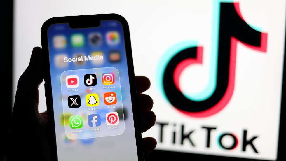 epa12674702 Social media applications displayed on a mobile phone alongside the TikTok logo displayed on a laptop screen in Liverpool, Britain, 23 January 2026. A proposal to ban under-16s from accessing social media in the UK will be considered in the House of Commons after peers in the House of Lords voted 261 to 150 in favour of an amendment to the Children’s Wellbeing and Schools Bill. If adopted, the amendment would require social media companies to implement strict and effective age checks in order to prevent underage users from signing up.  EPA/ADAM VAUGHAN