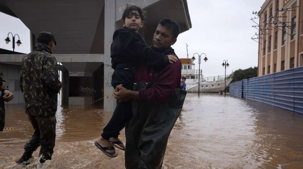 epa11317448 Inhabitants of the coastal islands of Lake Guaiba walk through the water after being rescued by the Brazilian army after flooding due to heavy rains, in Porto Alegre, Brazil, 03 May 2024. The floods have mainly affected the state of Rio Grande do Sul, including Porto Alegre, the regional capital, forcing more than 30,000 people to leaves their homes and causing at least 150 road closures.  EPA/Isaac Fontana