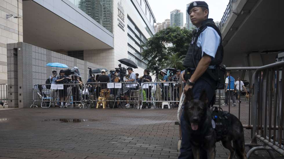 epa11435788 A police officer stands guard in front of a group of reporters, outside the West Kowloon Magistrates' Courts before a hearing on mitigation pleas, in Hong Kong, China, 25 June 2024. The court is set to hear mitigation pleas from the 45 defendants convicted under the national security law.  EPA/LEUNG MAN HEI