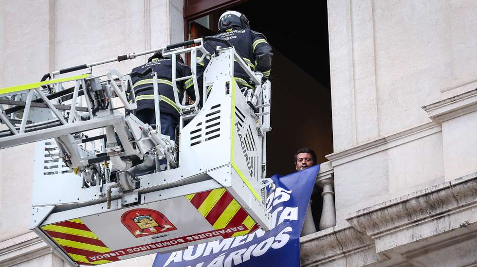 André Ventura e bombeiros retitram as tarjas colocadas pelos deputados do Chega, 29 de novembro de 2024. A sessão plenária de hoje foi marcada por um protesto, que incluiu a colocação de tarjas nas janelas da Assembleia da República, contra a aprovação ontem no parlamento do fim do corte de 5% nos salários dos titulares de cargos públicos. RODRIGO ANTUNES/LUSA