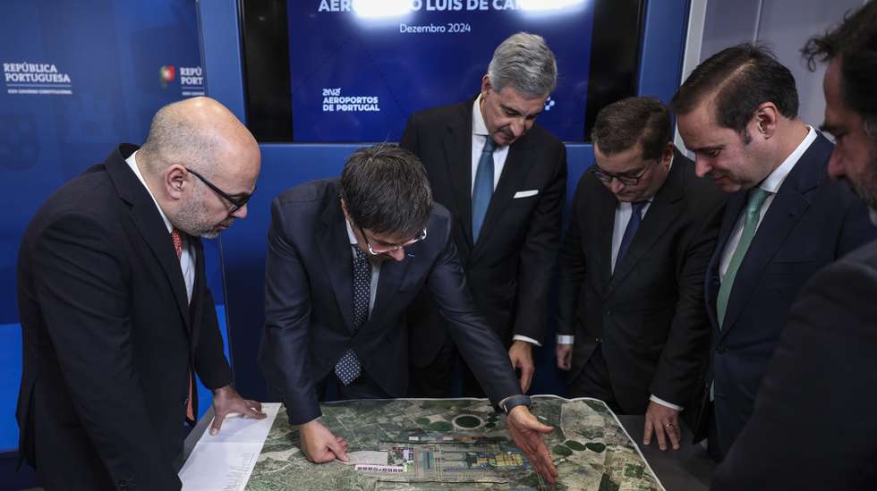 O ministro das Infraestruturas e Habitação, Miguel Pinto Luz (E), o ministro de Estado e das Finanças, Joaquim Miranda Sarmento (3-D), o presidente da ANA, José Luis Arnaut (3-E), e o presidente executivo da ANA, Thierry Ligonnière (2-E), observam o plano do aeroporto após receberem o Relatório Inicial (High Level Assumption Report) da concessionária ANA sobre o desenvolvimento da capacidade aeroportuária de Lisboa,  para iniciar formalmente negociações sobre a extensão do contrato de concessão e viabilizar a construção do novo Aeroporto Luís de Camões, em Alcochete, 17 de dezembro de 2024.  ANDRÉ KOSTERS/LUSA