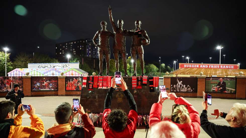 epa10931510 People take photographs of tributes left on the 'United Trinity' statue at Old Trafford following the announcement of the death of Sir Bobby Charlton, in Manchester, Britain, 21 October 2023. Sir Bobby Charlton was part of the 1966 World Cup winning England team, and won three league titles and the European Cup during his 17 years at Manchester United. His death at the age of 86 was announced on 21 October 2023.  EPA/ADAM VAUGHAN