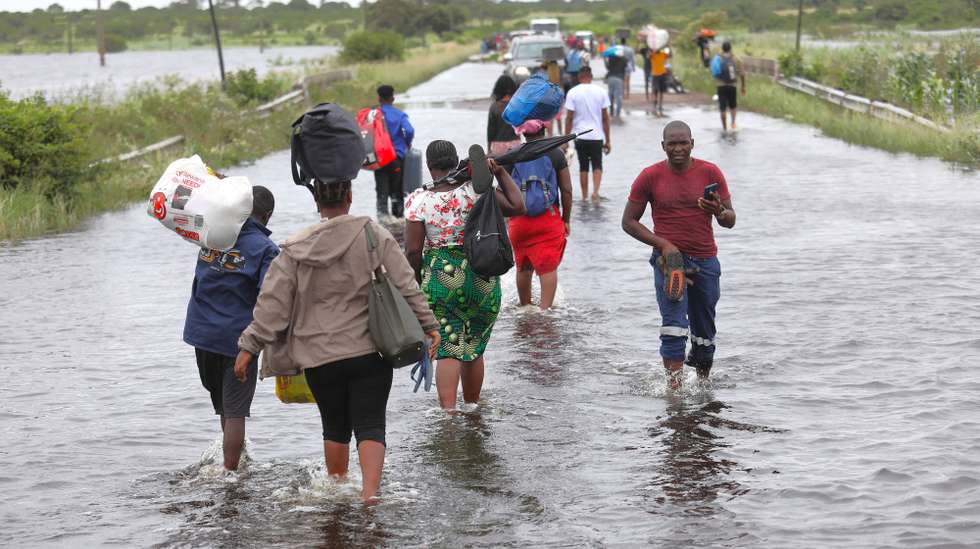 Populares atravessam uma estrada alagada, em Mahocha Homo, Maputo, 20 de janeiro de 2026. No meio de cheias sem memória em Moçambique a moto é o último transporte em Mahocha Homo, a meio caminho entre Manhiça e Palmeiras, onde as águas de um pequeno riacho, que mal alimentava os campos agrícolas, galgaram a estrada. (ACOMPANHA TEXTO DA LUSA DO DIA 24 DE JANEIRO DE 2026). LUÍSA NHANTUMBO/LUSA