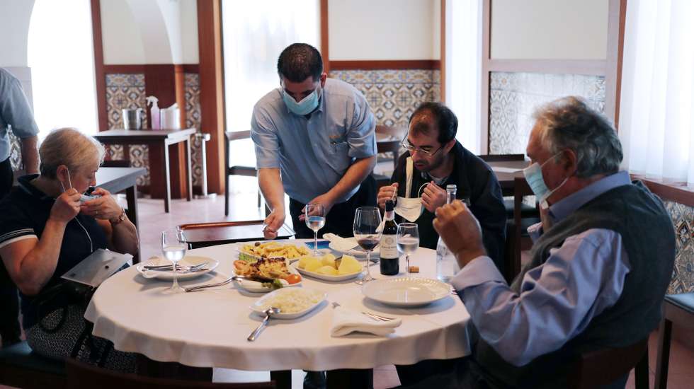 Um empregado com uma máscara deproteção respiratória serve uma refeição a clientes no restaurante O Gaveto , em Matosinhos, 18 de maio de 2020. O presidente do Turismo do Porto e Norte de Portugal, Luís Pedro Martins e a presidente da Câmara Municipal de Matosinhos, Luísa Salgueiro (ausentes na foto), assinalaram em conjunto a reabertura da restauração após o alivio das medidas de emergência devido à situação epidemiológica da covid-19. ESTELA SILVA/LUSA