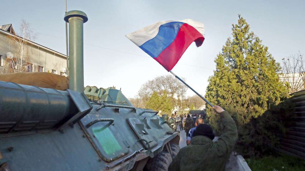 epa04136507 A Crimea's self-defense units member carries a Russian National flag during an assault on the last Ukrainian military base, which has not surrendered after the annexation of Crimea by Russia in Belbek, Crimea, Ukraine, 22 March 2014. Crimean Premier Sergey Aksenov stressed that the base had been liberated from 'foreign troops'. In recent days, Russia has sought to clear out the last few pockets of resistance by browbeating dispirited Ukrainian troops into surrender.  EPA/SERGEI ILNITSKY