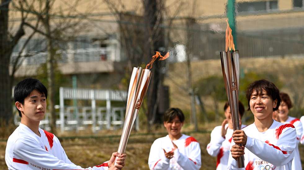 epa09095171 Japanese torchbearer Azusa Iwashimizu (R), a member of Japan women's national football team, passes the Olympic flame to the high school student Asato Owada at a torch kiss point during the torch relay grand start outside J-Village National Training Centre in Naraha, Fukushima Prefecture, Japan, 25 March 2021.  EPA/PHILIP FONG / POOL