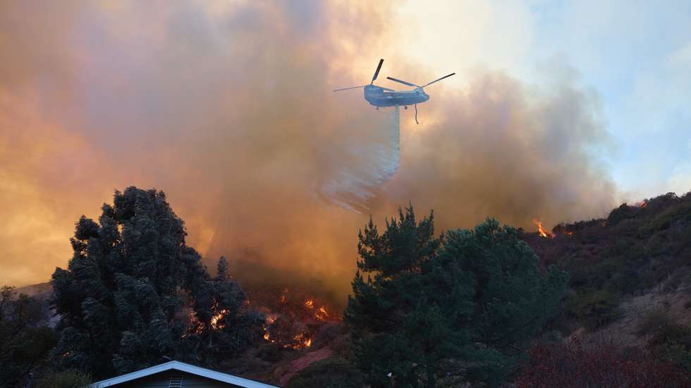epaselect epa11819202 A helicopter does a water drop over a home during the Palisades wildfire in Los Angeles, California, USA, 11 January 2025. Thousands of firefighting and emergency personnel are involved in response efforts, as multiple wildfires are continuing to burn across thousands of acres in Southern California, destroying thousands of homes and forcing people to evacuate areas throughout the Los Angeles area.  EPA/ALLISON DINNER