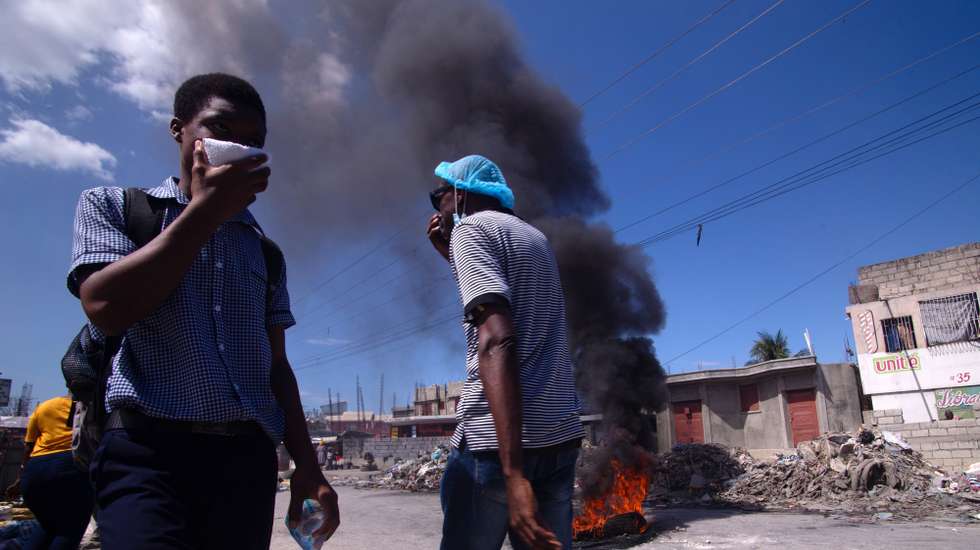 epaselect epa11922752 People walk near a burning tire during a new day of mobilizations against insecurity in the Tabarre area of Port-au-Prince, Haiti, 24 February 2024.  EPA/MENTOR DAVID LORENS
